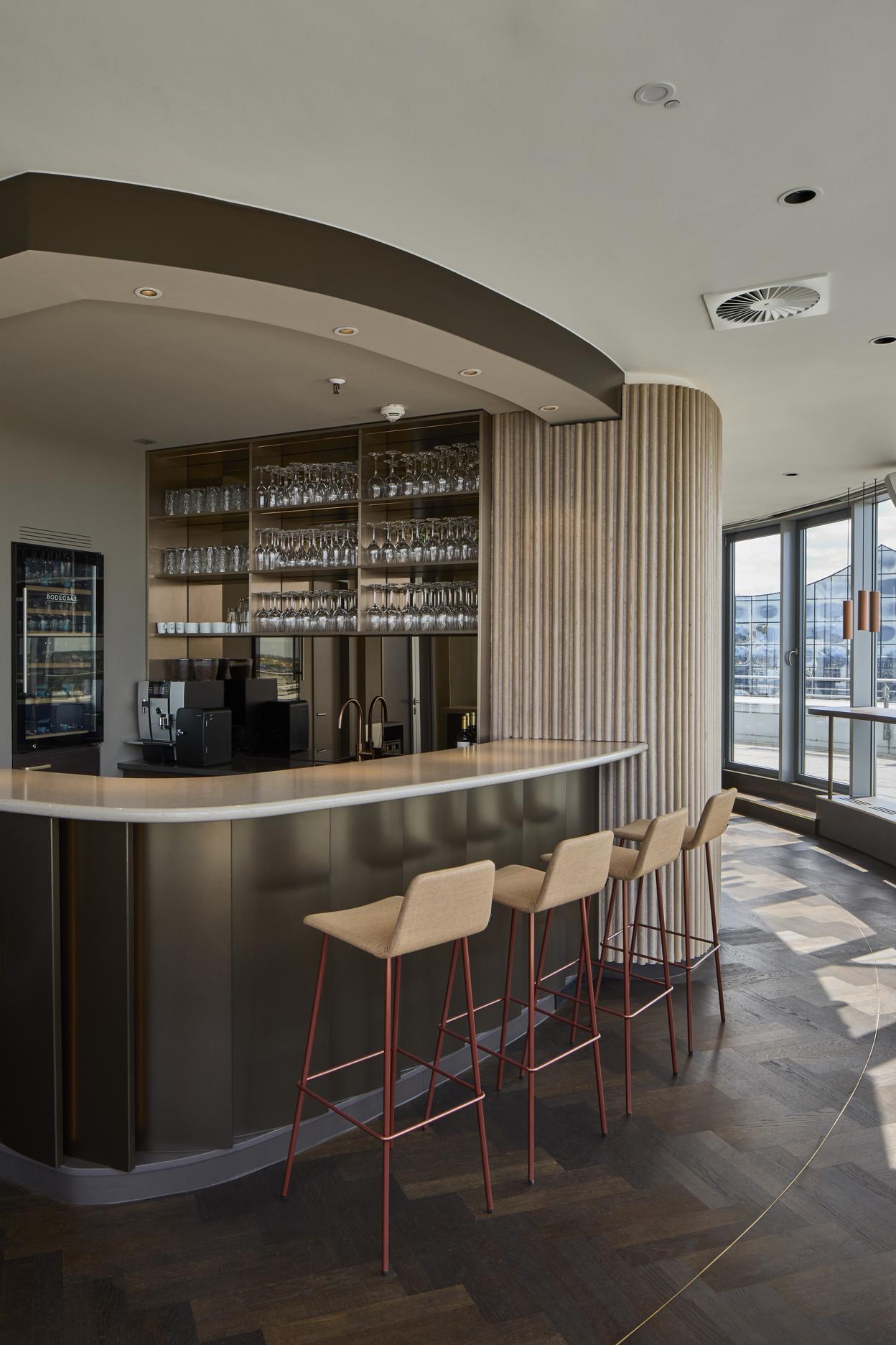 Exklusiver Innenausbau einer Bar mit maßgefertigter Theke Moderne Bar mit Glasregalen, Theke und stilvollen Barhockern in heller Umgebung