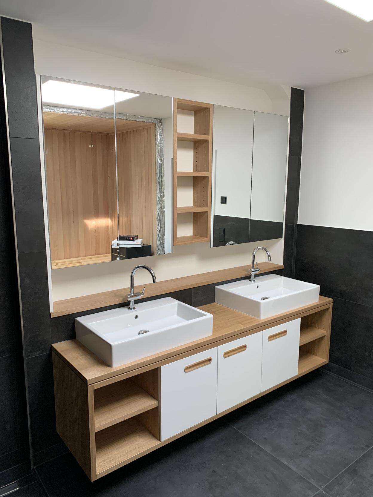 Maßgefertigte Badmöbel mit Doppelwaschbecken Eine maßgefertigte Badmöbel-Lösung mit zwei Waschbecken, Holzunterschrank und integrierten Regalfächern. Über den Waschbecken befinden sich große Spiegel. Badmöbel nach Maß.