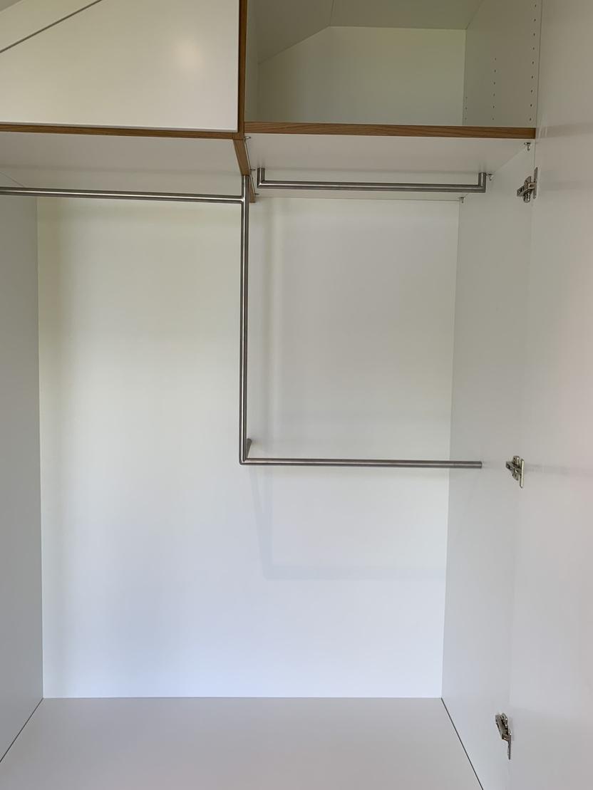 Innenausstattung eines Einbauschranks mit Kleiderstangen Innenansicht eines maßgefertigten Einbauschranks mit zwei versetzten Edelstahl-Kleiderstangen in L-Form, weiß beschichteten Flächen und oberem Stauraumfach