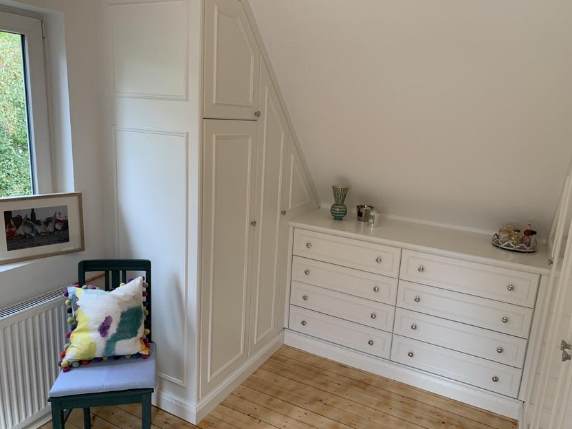 Zimmer mit Dachschrägenschränken und Kommode Ein helles, gemütliches Zimmer mit weißen Einbauschränken, die sich an die Dachschräge anpassen.