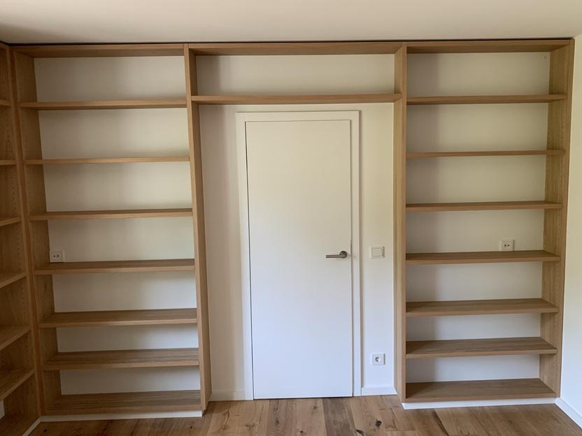 Einbau-Regalwand aus Eiche mit Türintegration Individuell gefertigtes Regal aus hellem Eichenholz, das eine Zimmertür vollständig einfasst, mit offenen Regalfächern links, rechts und oberhalb der Tür