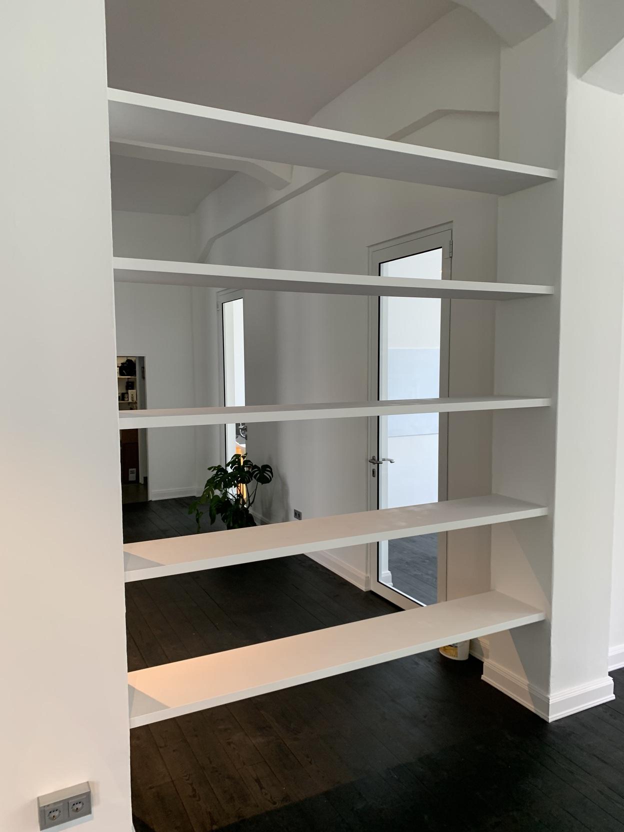 Offenes Wandregal als Raumteiler Weißes, wandintegriertes Regal mit sechs durchgehenden, offenen Böden, eingebaut zwischen zwei Räumen mit dunklem Holzboden